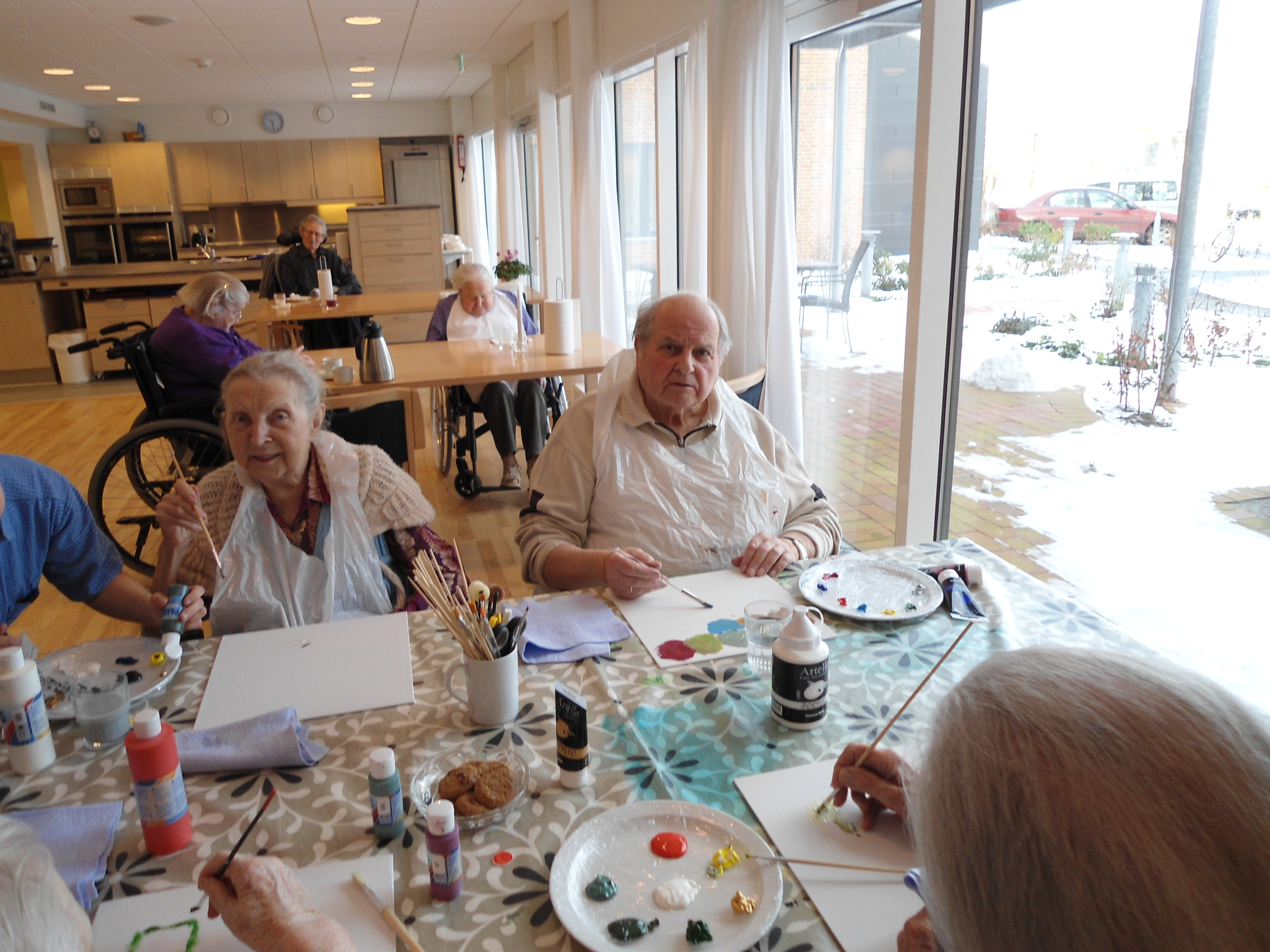 To ældre mennesker sidder og maler billeder i et daghjem